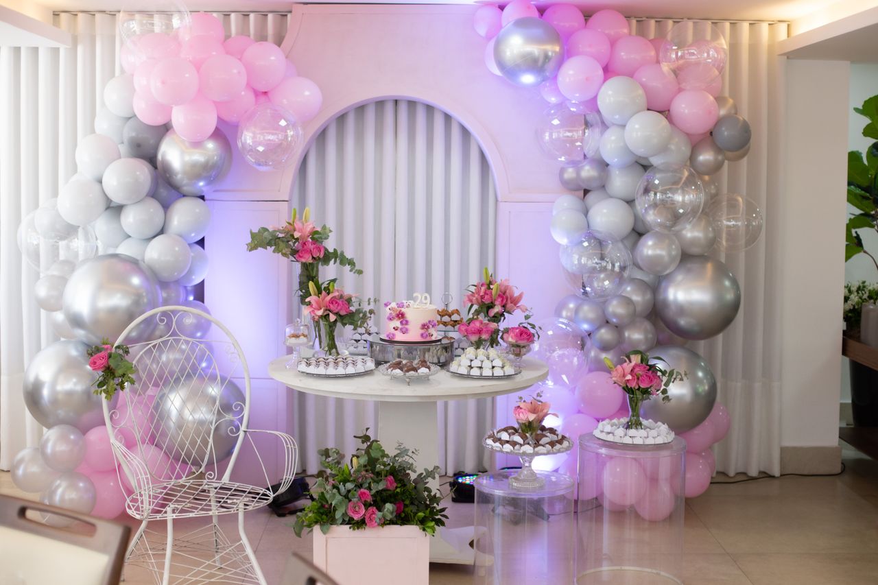About Beautiful birthday celebration setup with pink and silver balloons, floral arrangements, and a stylish cake display.