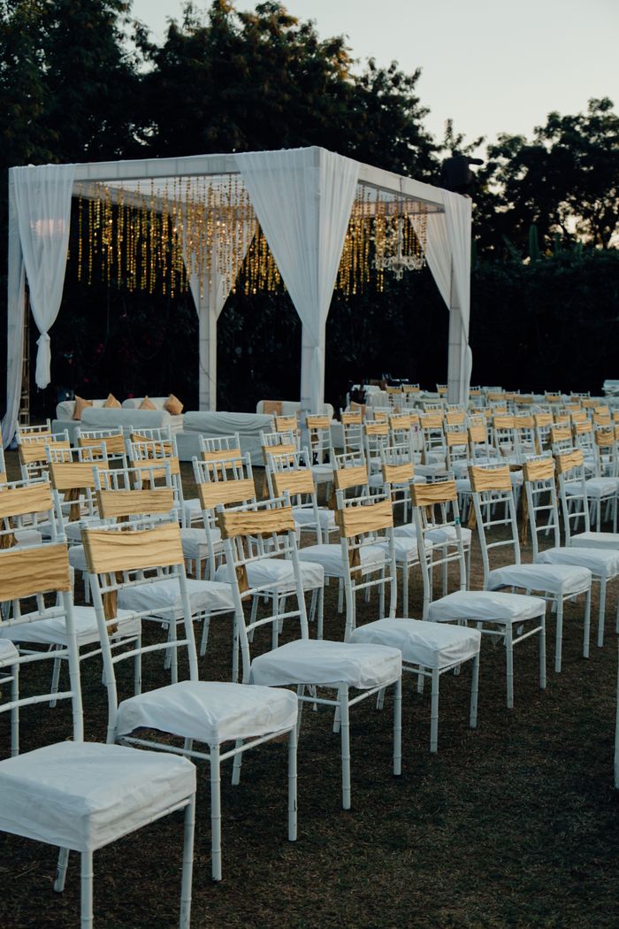 About Charming outdoor wedding venue with white chairs and altar under evening sky.